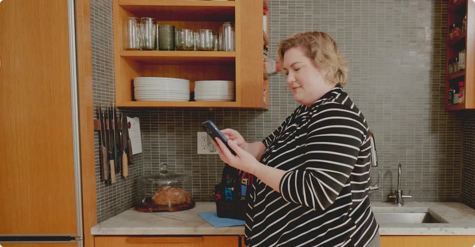 A person looking at their phone and smiling, in a home kitchen setting.